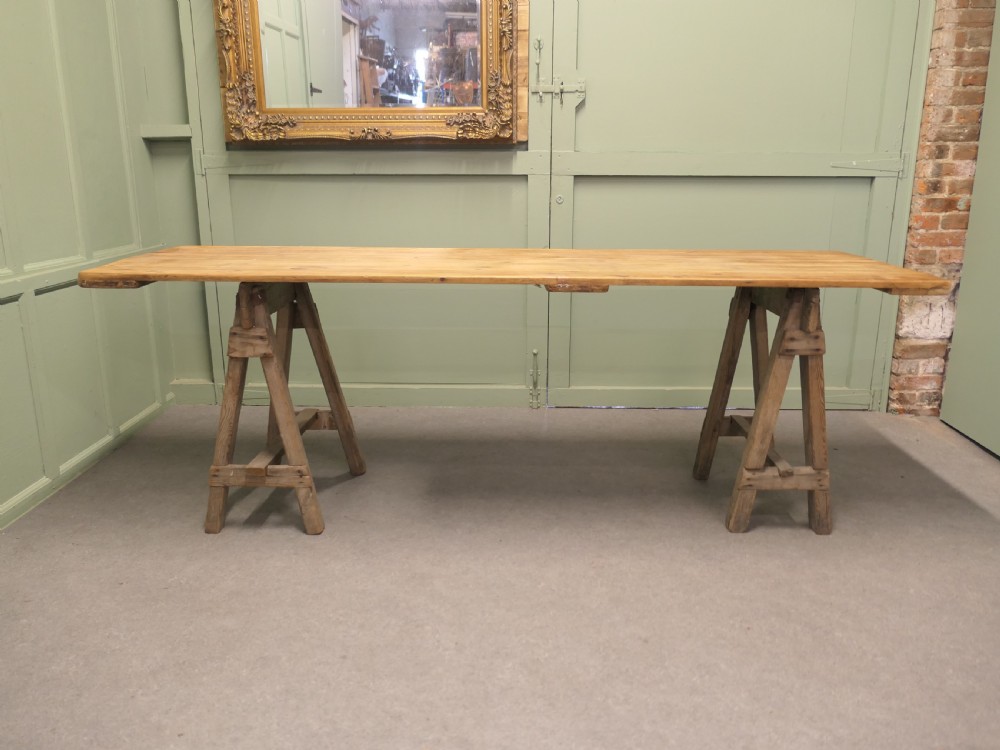 A long rustic elm harvest table featuring a simple solid plank top supported by twin wooden A-frame trestle legs.