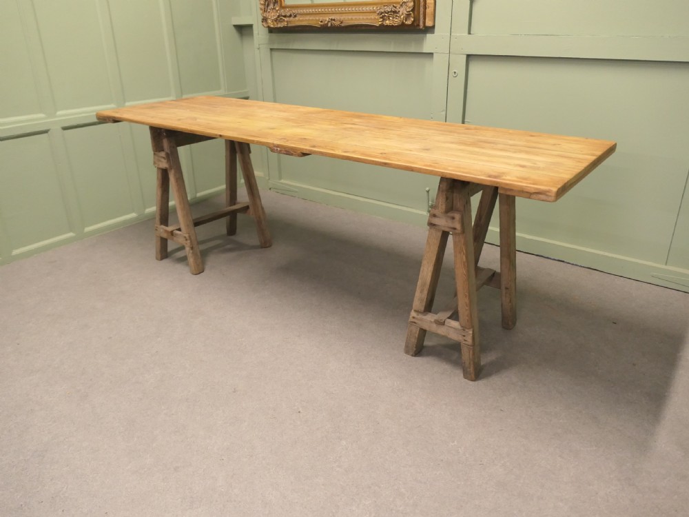 A long rustic elm harvest table featuring a simple solid plank top supported by twin wooden A-frame trestle legs. View III