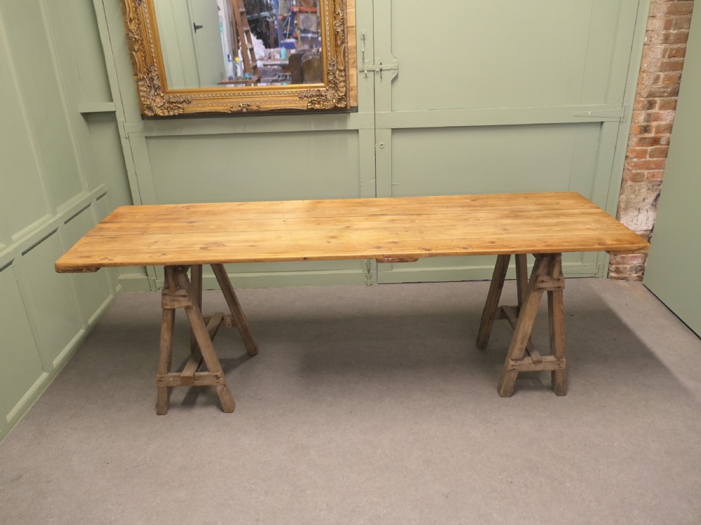 A long rustic elm harvest table featuring a simple solid plank top supported by twin wooden A-frame trestle legs. View V