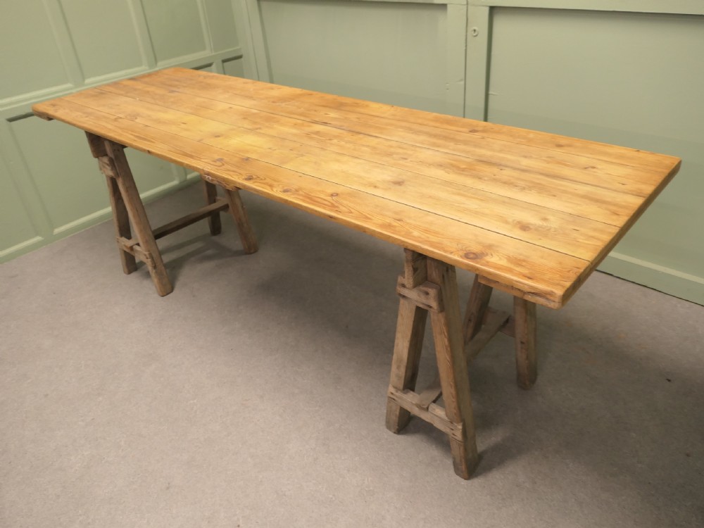 A long rustic elm harvest table featuring a simple solid plank top supported by twin wooden A-frame trestle legs. View VI
