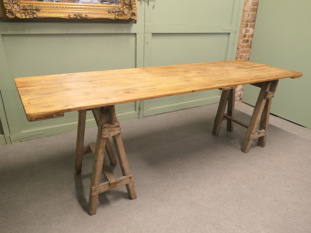 A long rustic elm harvest table featuring a simple solid plank top supported by twin wooden A-frame trestle legs. View VII