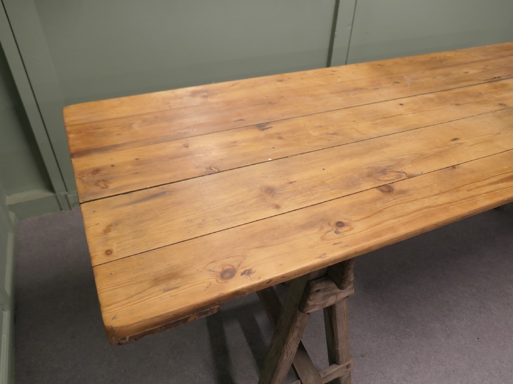 A long rustic elm harvest table featuring a simple solid plank top supported by twin wooden A-frame trestle legs. View VIII