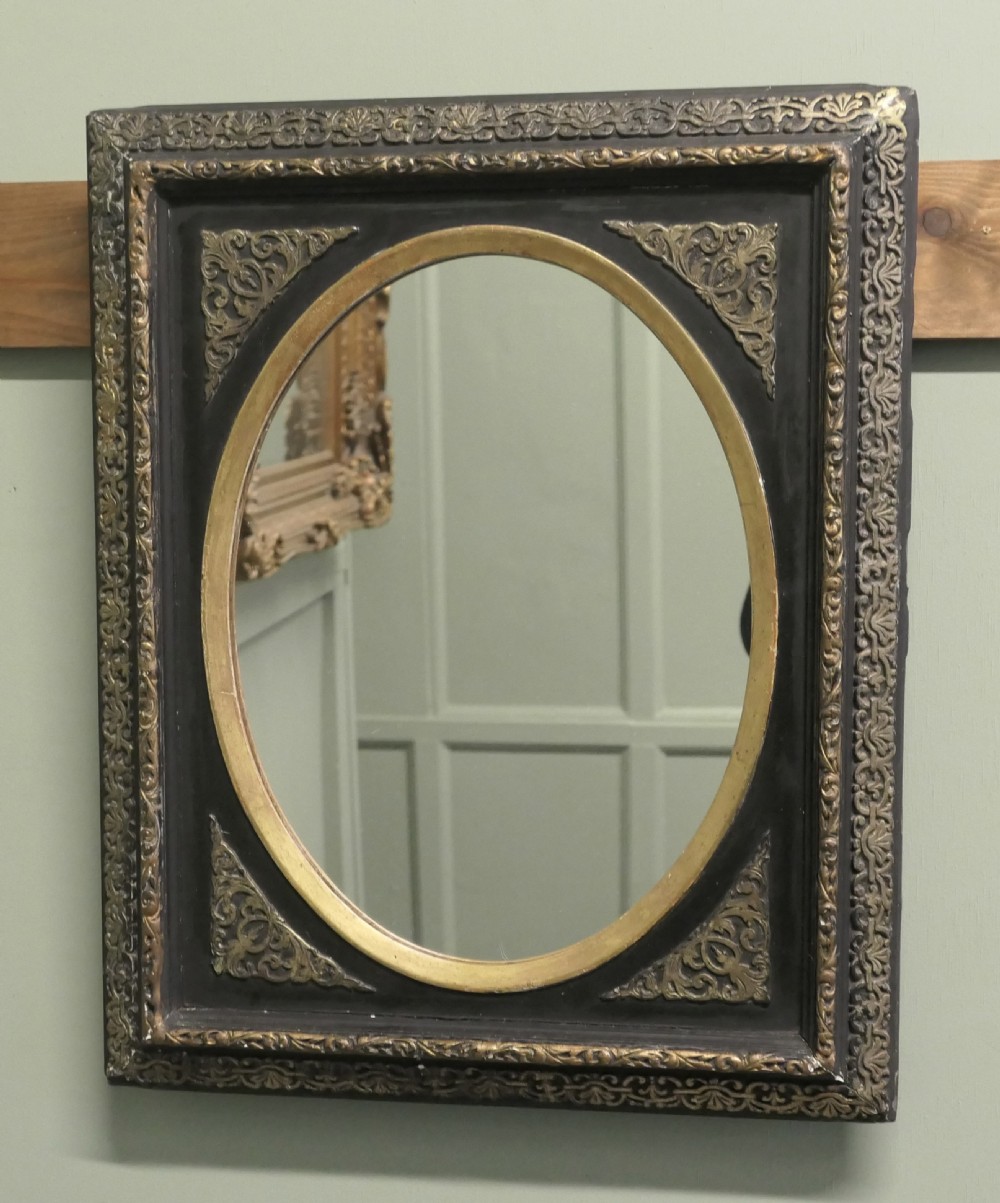 A rectangular black lacquered wall mirror featuring intricate gilt brass floral borders, ornate corner mounts, and an inner oval frame housing a glass mirror.