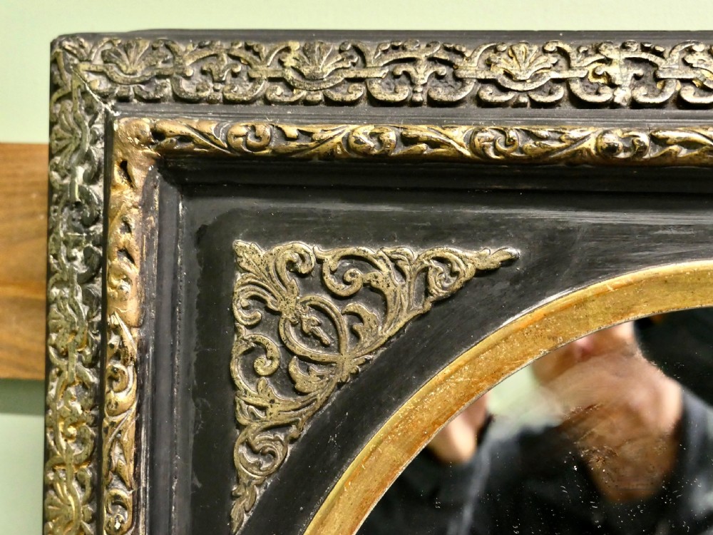 A rectangular black lacquered wall mirror featuring intricate gilt brass floral borders, ornate corner mounts, and an inner oval frame housing a glass mirror. View IV