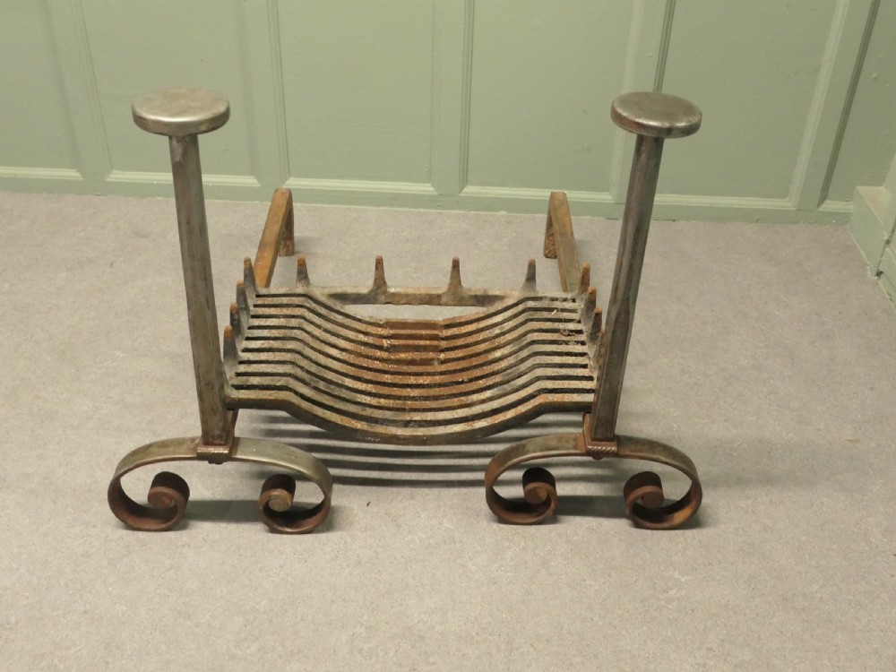 A heavy dark iron fireplace grate featuring scrolled front feet, twin upright pillar posts with flat circular tops, and a curved central log basket. View III