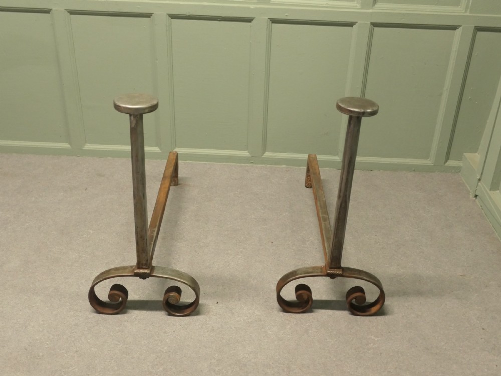 A heavy dark iron fireplace grate featuring scrolled front feet, twin upright pillar posts with flat circular tops, and a curved central log basket. View V