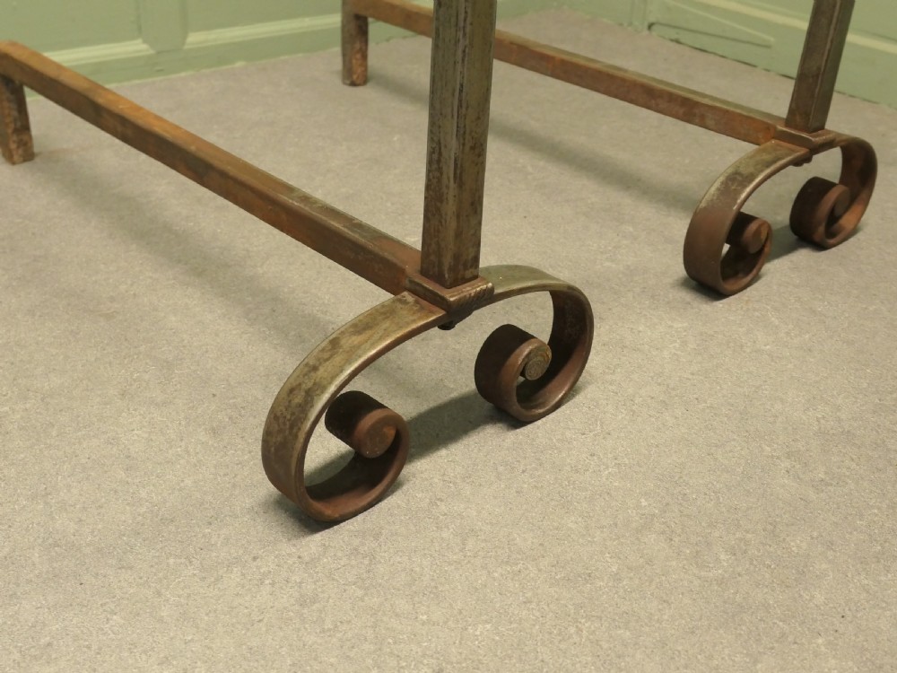 A heavy dark iron fireplace grate featuring scrolled front feet, twin upright pillar posts with flat circular tops, and a curved central log basket. View VI