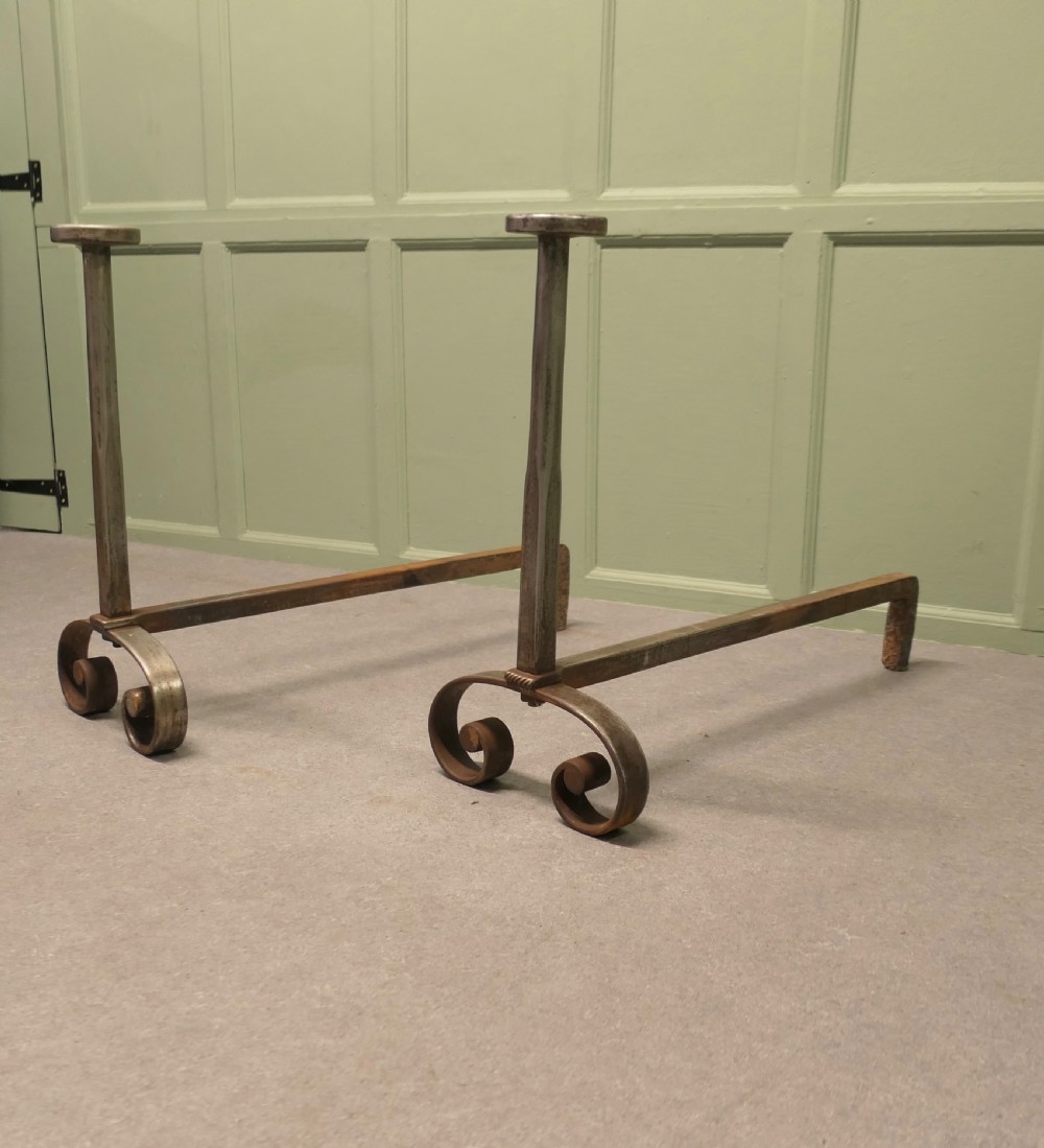 A heavy dark iron fireplace grate featuring scrolled front feet, twin upright pillar posts with flat circular tops, and a curved central log basket. View VII