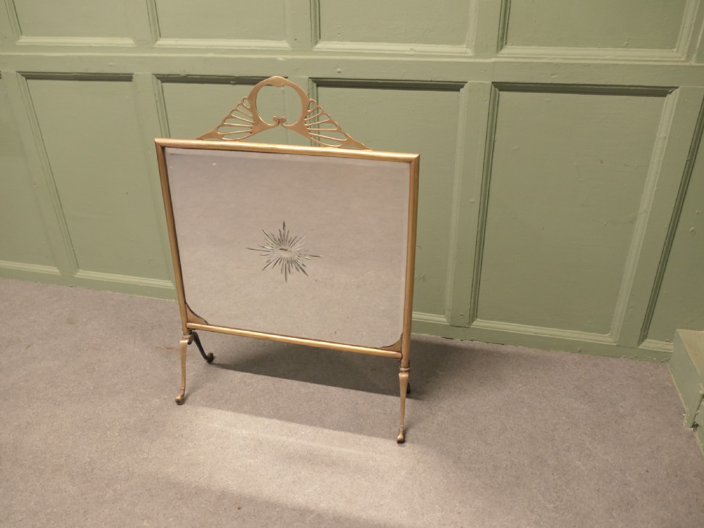 An Art Deco brass fire screen featuring a mirrored glass panel with a central etched sunburst motif and splayed feet. View II