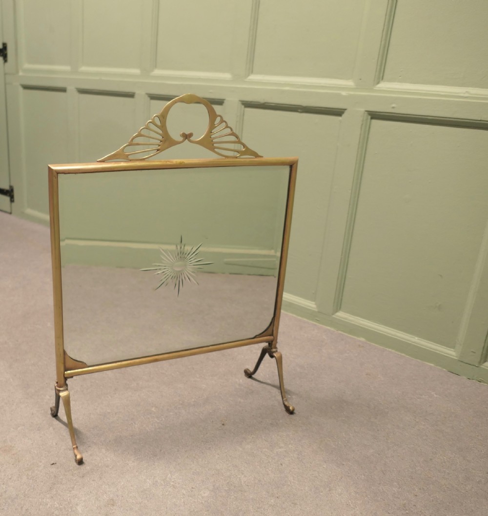 An Art Deco brass fire screen featuring a mirrored glass panel with a central etched sunburst motif and splayed feet. View III