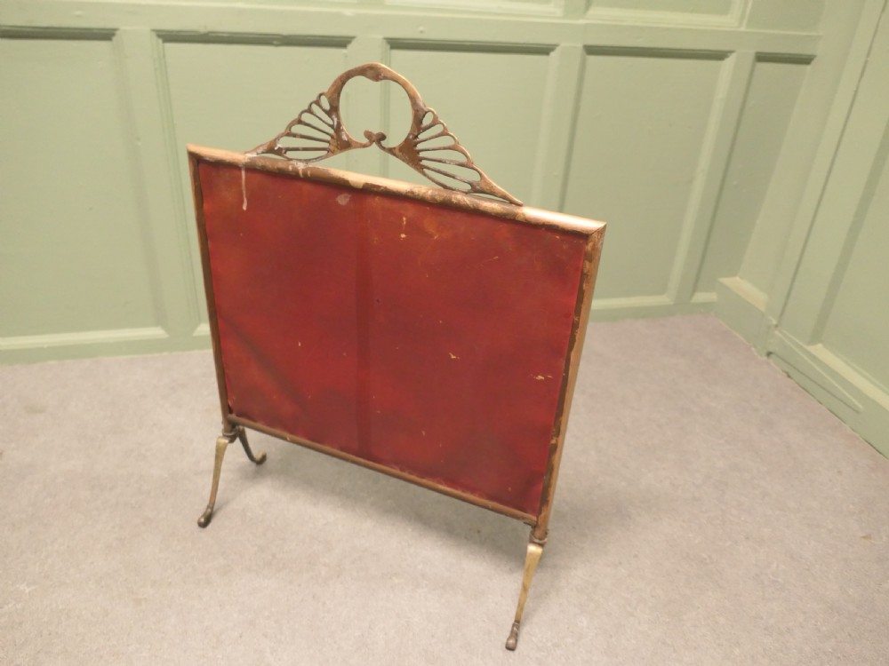 An Art Deco brass fire screen featuring a mirrored glass panel with a central etched sunburst motif and splayed feet. View IV