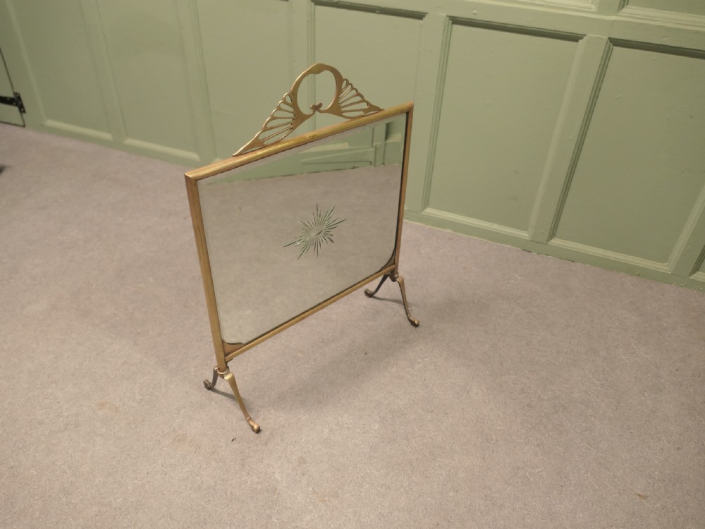 An Art Deco brass fire screen featuring a mirrored glass panel with a central etched sunburst motif and splayed feet. View VI