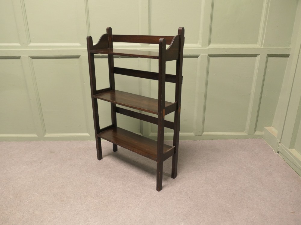 A dark oak three-shelf open bookcase with shaped side profiles and horizontal support rails.