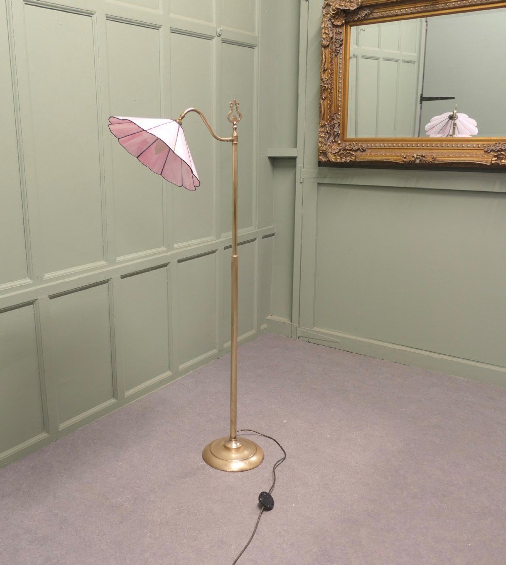 An Edwardian brass floor standing reading lamp featuring a swivel arm, weighted circular base, and a scalloped pink shade.