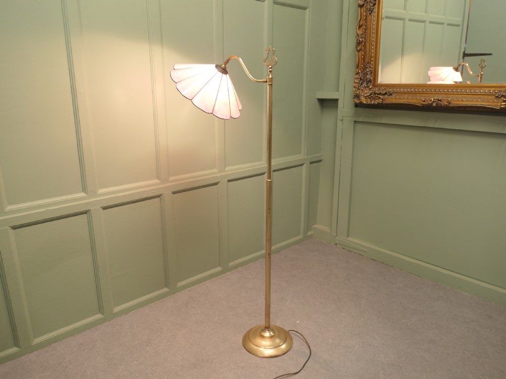 An Edwardian brass floor standing reading lamp featuring a swivel arm, weighted circular base, and a scalloped pink shade. View II