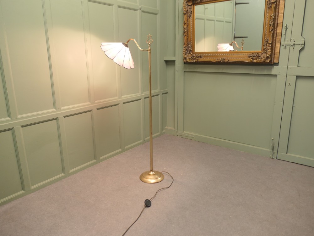 An Edwardian brass floor standing reading lamp featuring a swivel arm, weighted circular base, and a scalloped pink shade. View V