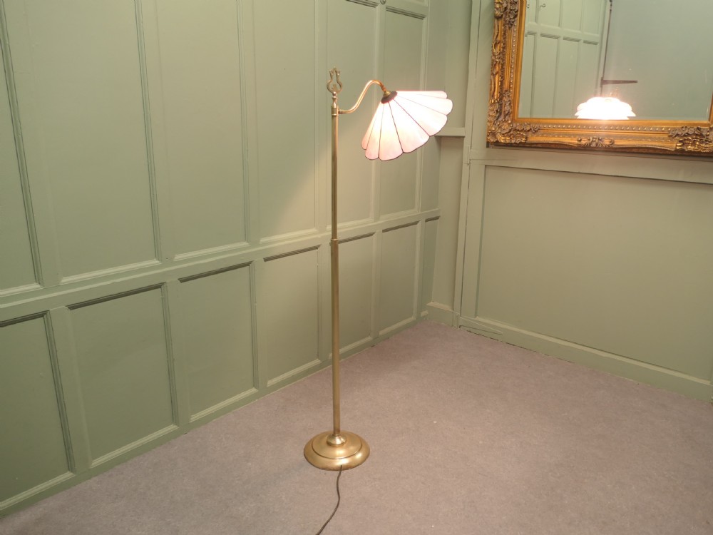 An Edwardian brass floor standing reading lamp featuring a swivel arm, weighted circular base, and a scalloped pink shade. View VII
