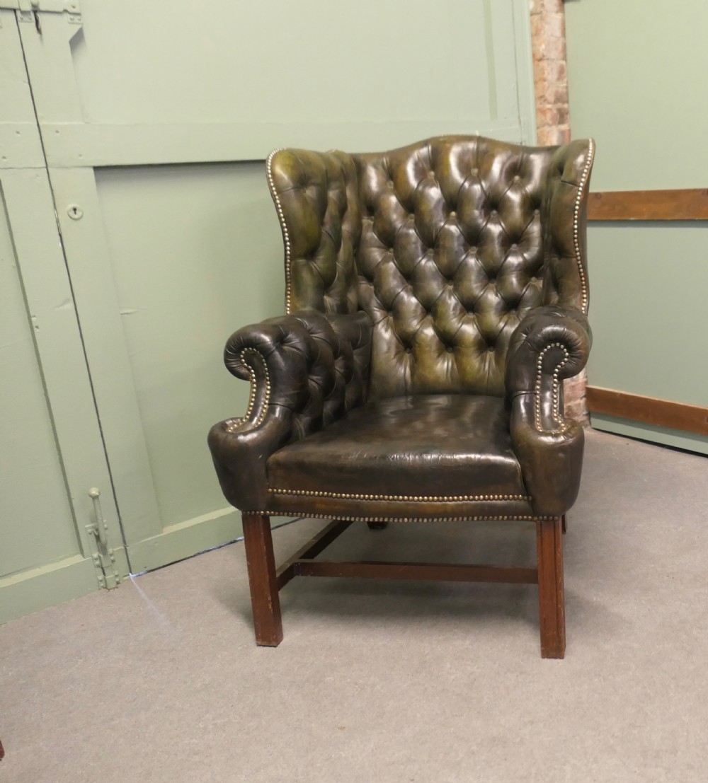 A pair of olive green leather wingback armchairs featuring deep button tufting, brass studding, and square wooden legs. View II