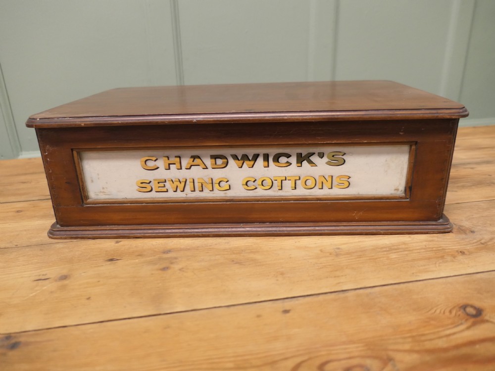 A two-drawer timber haberdashery display cabinet with turned wooden knobs and glass drawer fronts featuring gold lettering that reads Chadwicks Sewing Cottons. View II
