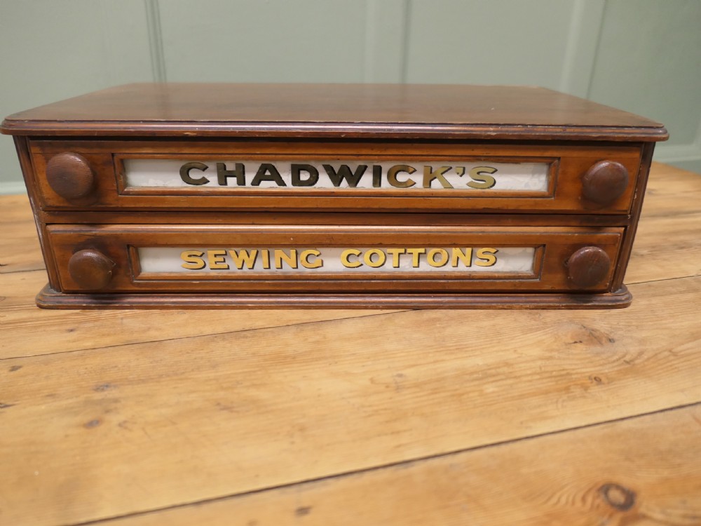 A two-drawer timber haberdashery display cabinet with turned wooden knobs and glass drawer fronts featuring gold lettering that reads Chadwicks Sewing Cottons. View III