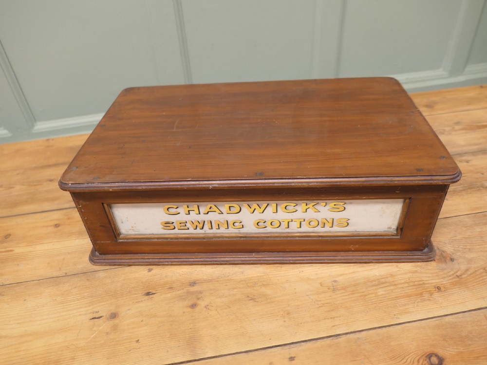 A two-drawer timber haberdashery display cabinet with turned wooden knobs and glass drawer fronts featuring gold lettering that reads Chadwicks Sewing Cottons. View V