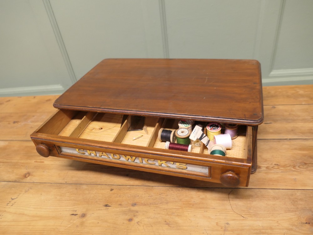 A two-drawer timber haberdashery display cabinet with turned wooden knobs and glass drawer fronts featuring gold lettering that reads Chadwicks Sewing Cottons. View VI