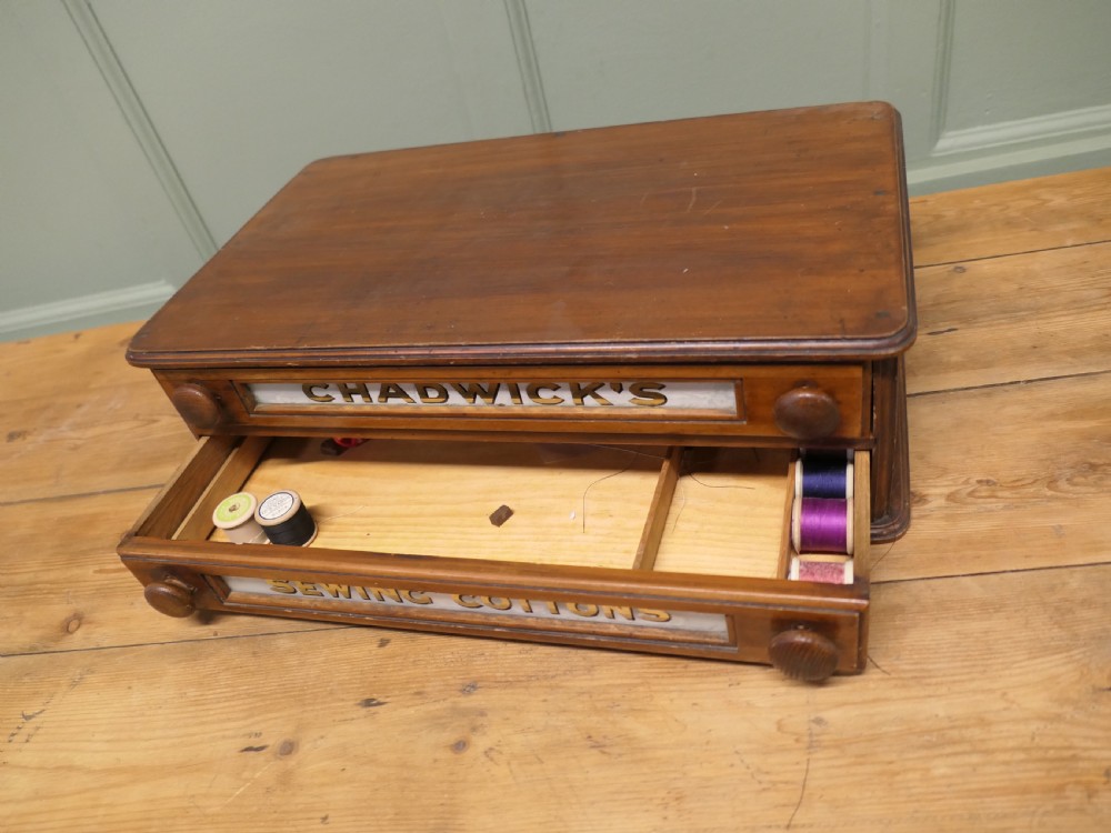 A two-drawer timber haberdashery display cabinet with turned wooden knobs and glass drawer fronts featuring gold lettering that reads Chadwicks Sewing Cottons. View VII