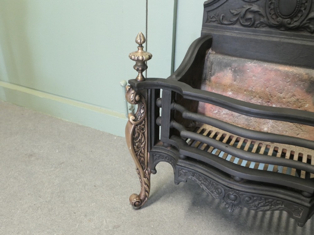 A freestanding cast iron fire basket with brass scroll legs, urn finials, an ornate crest backplate, and an internal firebrick lining. View III