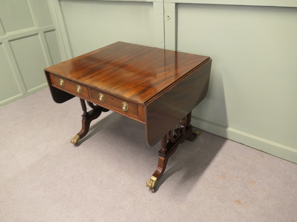 A Regency mahogany sofa table featuring two drop leaves, dual frieze drawers with brass handles, and lyre-shaped end supports terminating in brass lion paw castors. View II