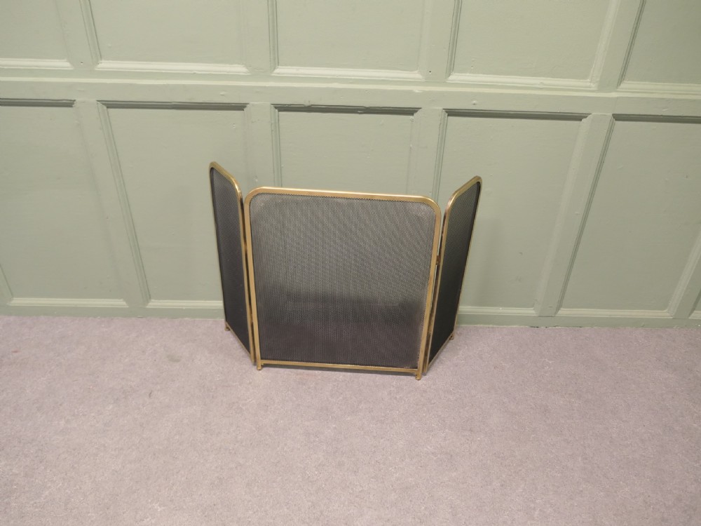 A three-panel folding fire guard featuring a tubular brass frame with black wire mesh screen inserts.