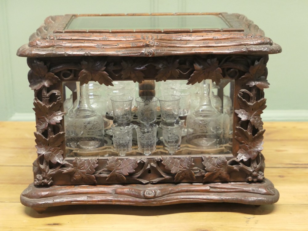 A carved wooden Black Forest liqueur box with glass panels enclosing etched glass decanters and small glasses.