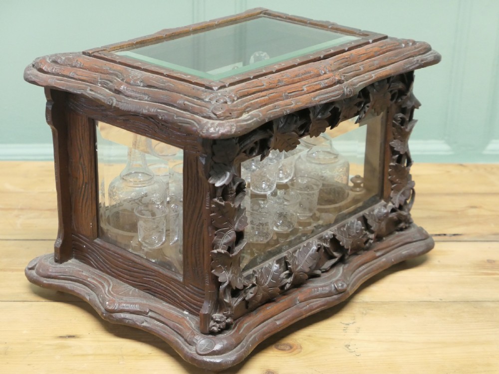 A carved wooden Black Forest liqueur box with glass panels enclosing etched glass decanters and small glasses. View V
