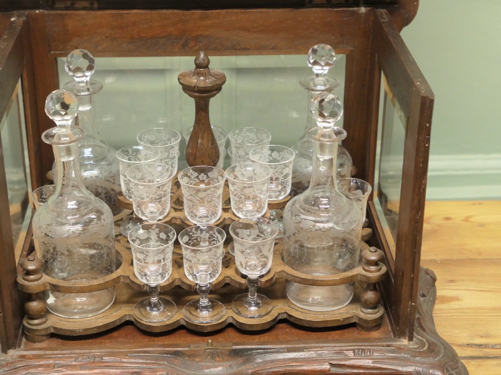 A carved wooden Black Forest liqueur box with glass panels enclosing etched glass decanters and small glasses. View VII