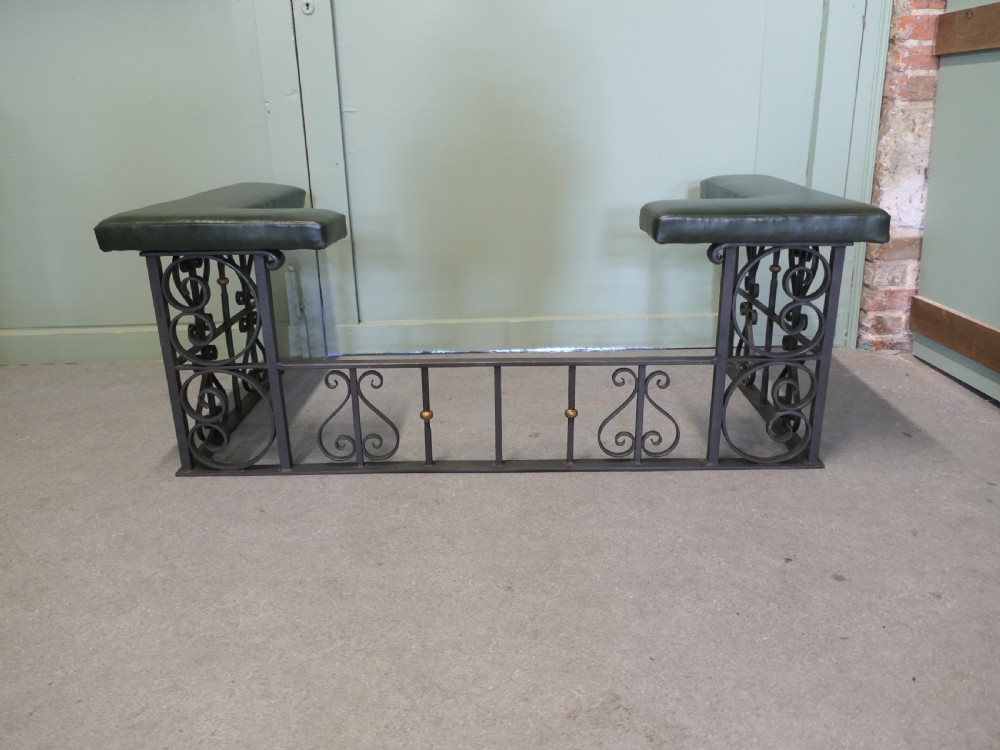 A black wrought iron club fender featuring scrollwork framing, brass details, and two green leather L-shaped corner cushions. View II
