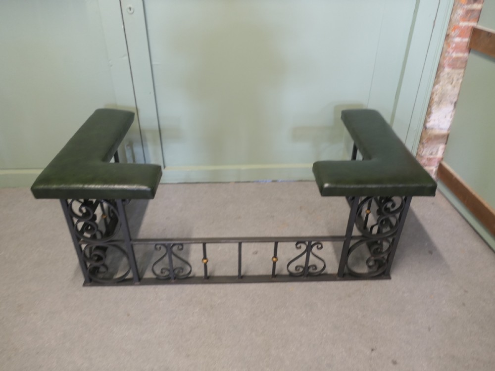 A black wrought iron club fender featuring scrollwork framing, brass details, and two green leather L-shaped corner cushions. View III