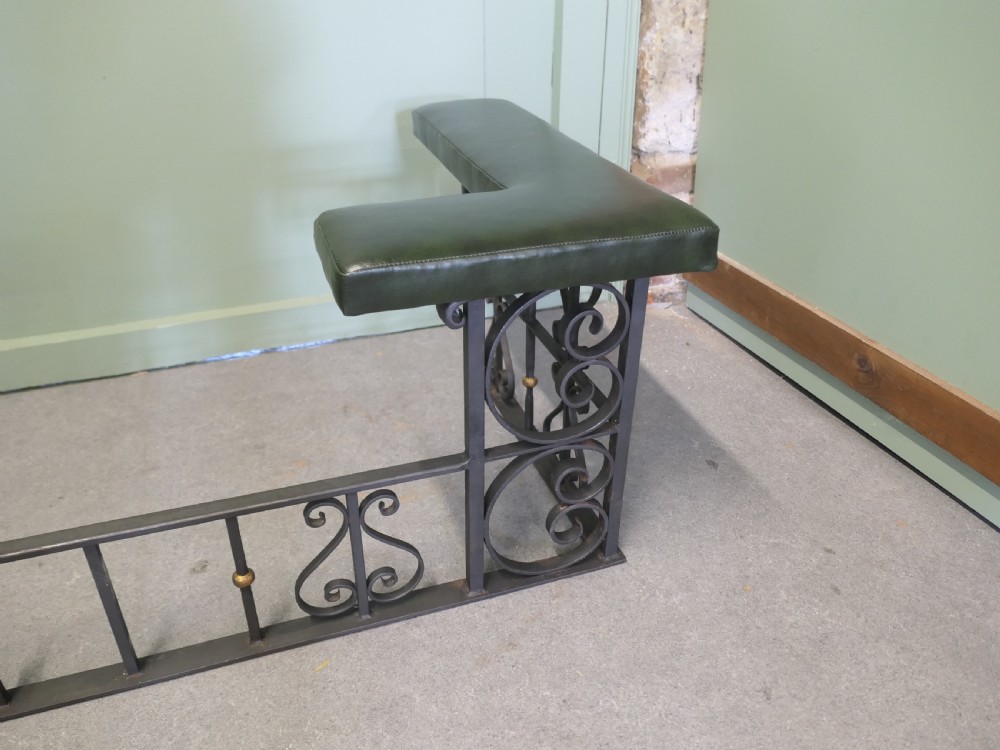 A black wrought iron club fender featuring scrollwork framing, brass details, and two green leather L-shaped corner cushions. View IV