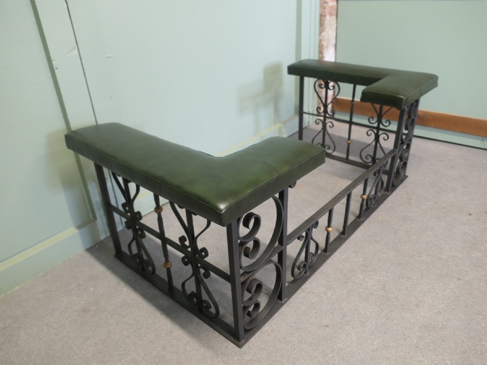 A black wrought iron club fender featuring scrollwork framing, brass details, and two green leather L-shaped corner cushions. View V