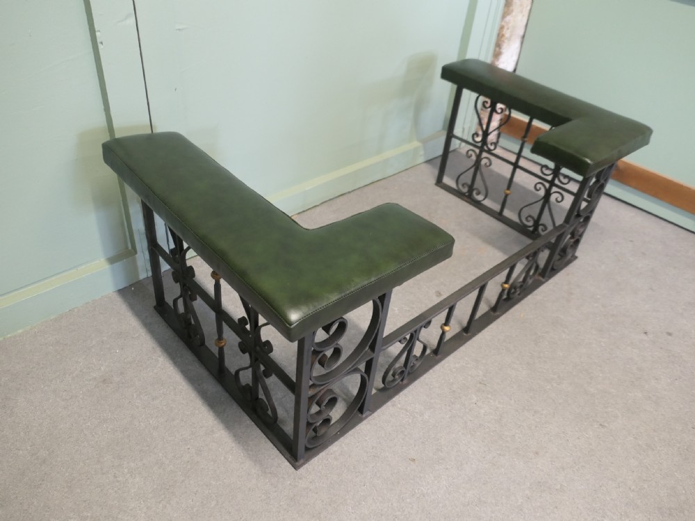 A black wrought iron club fender featuring scrollwork framing, brass details, and two green leather L-shaped corner cushions. View VI