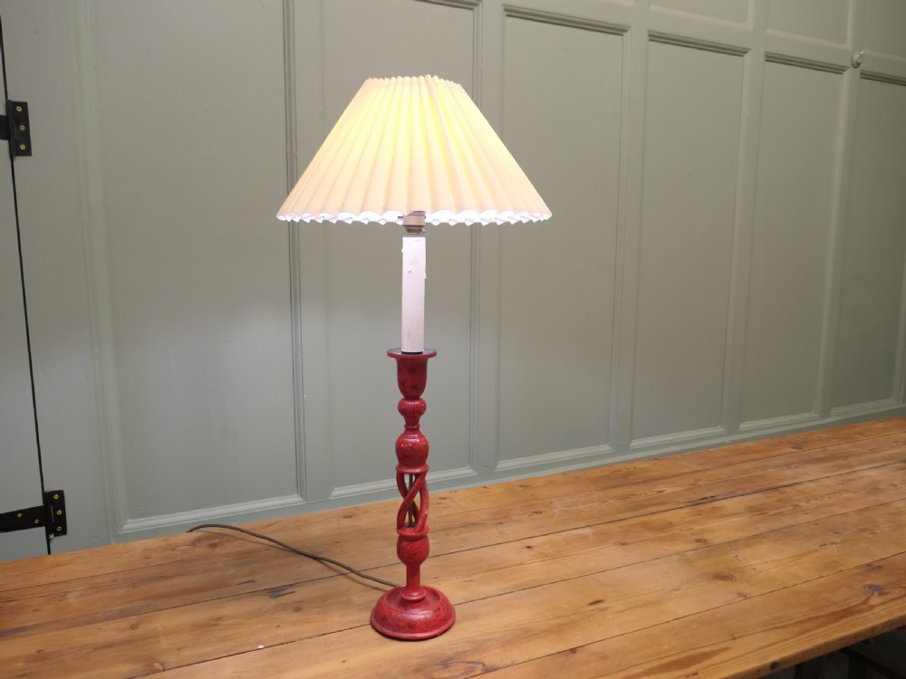 A red painted wooden table lamp featuring an open barley twist stem and a pleated cream lampshade.