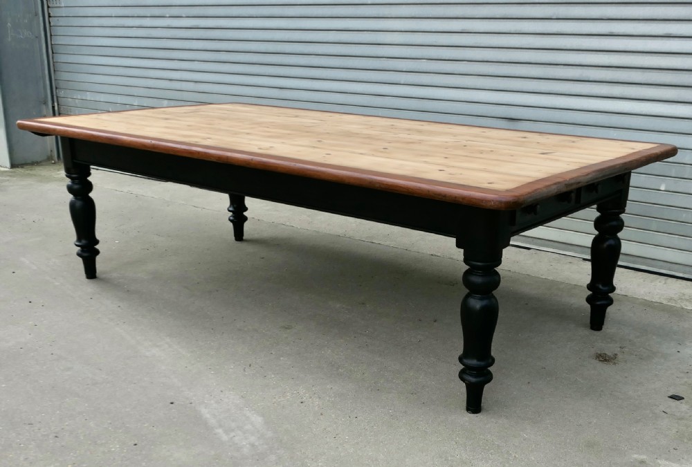 A large Victorian pine farmhouse dining table featuring a natural wood top with dark trim and a black painted base with four turned legs.