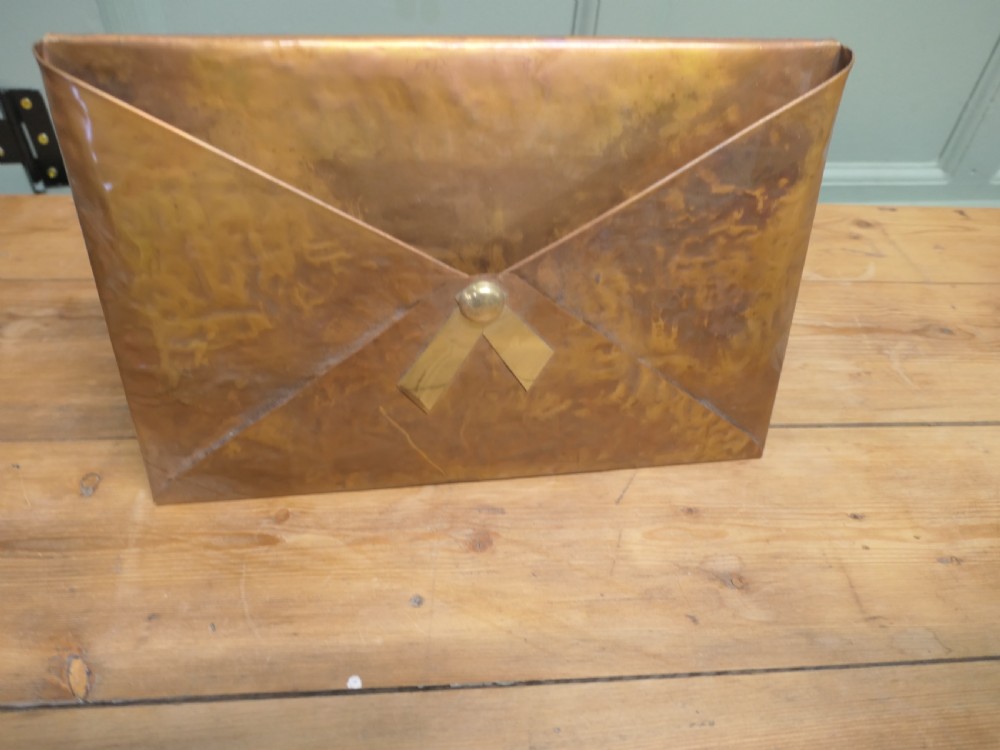 A beaten copper desk letter rack shaped like an envelope with a brass central stud detailing.