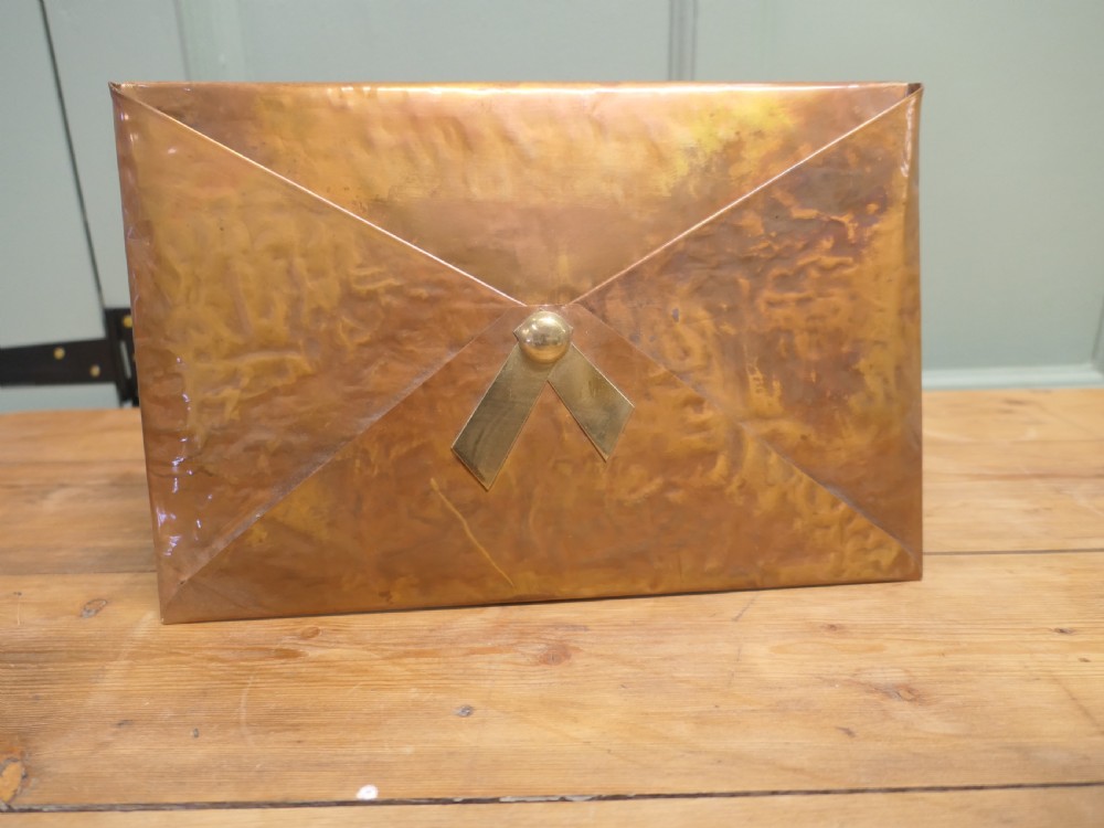 A beaten copper desk letter rack shaped like an envelope with a brass central stud detailing. View II