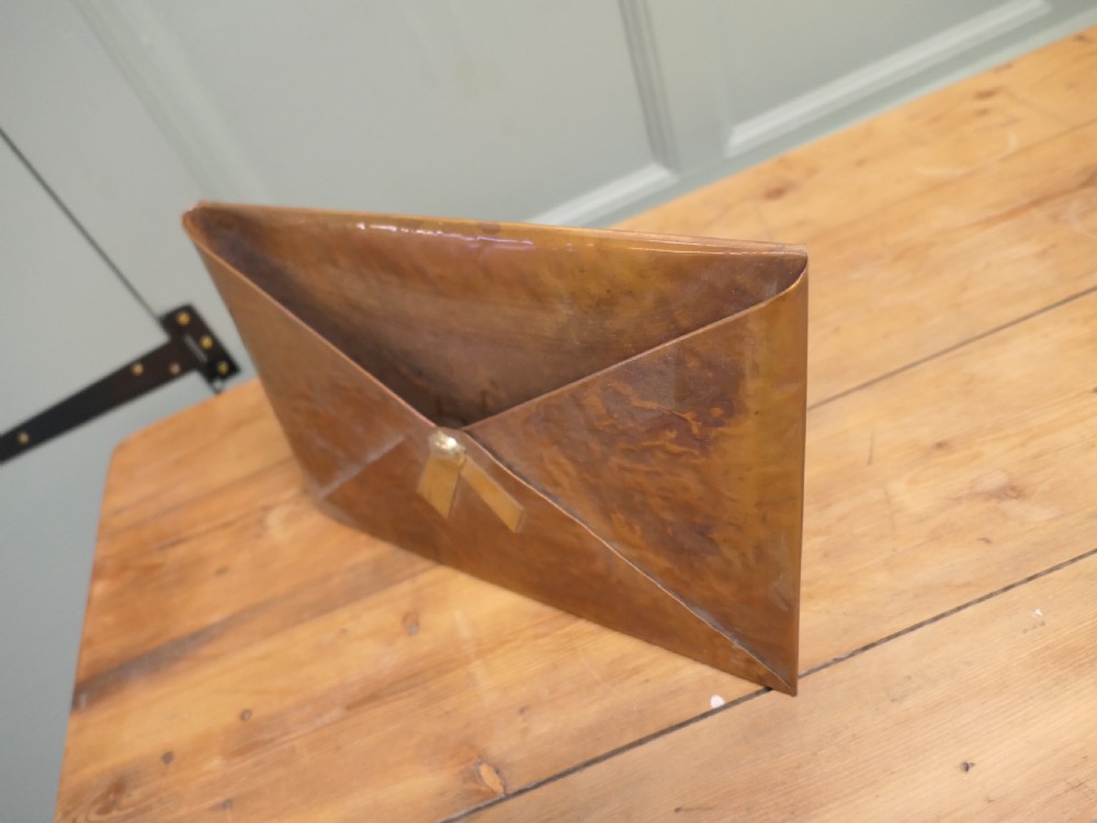 A beaten copper desk letter rack shaped like an envelope with a brass central stud detailing. View V