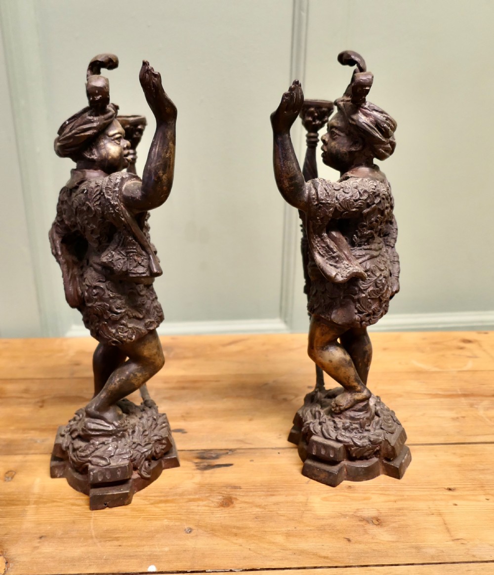 A pair of dark patinated cast brass figural candlesticks depicting standing figures in patterned tunics and turbans holding raised candle nozzles. View III