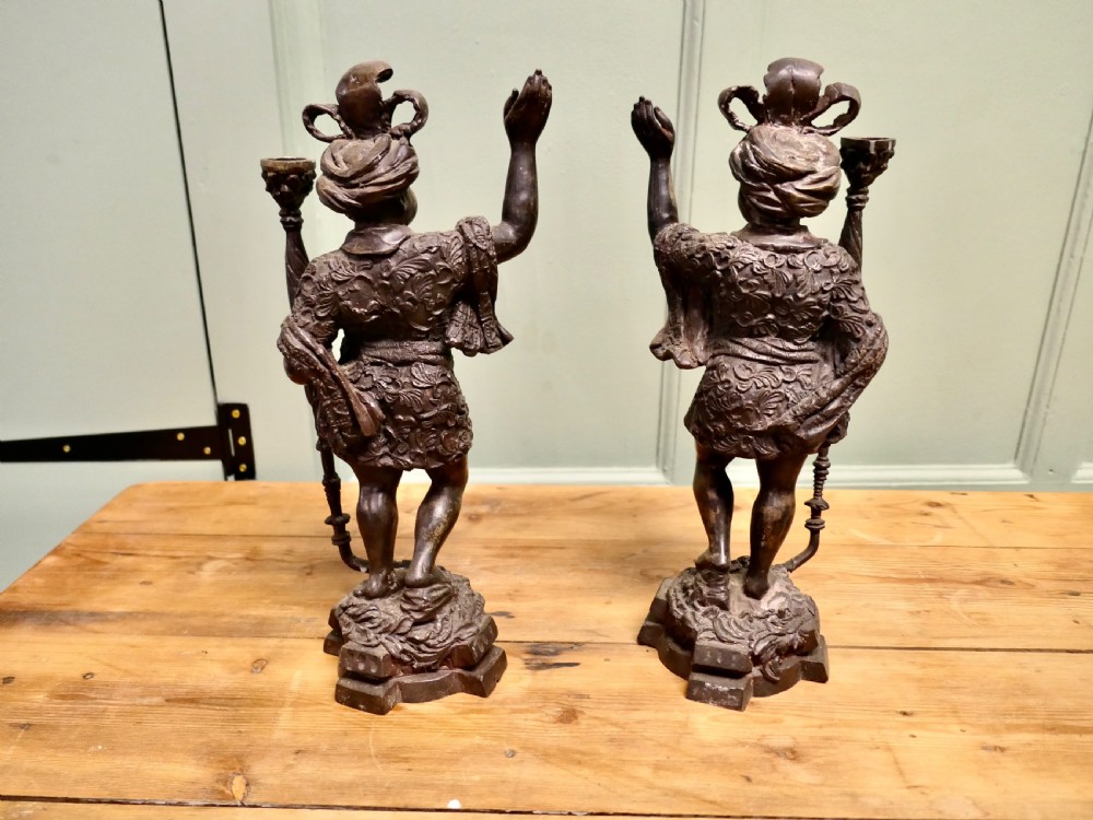 A pair of dark patinated cast brass figural candlesticks depicting standing figures in patterned tunics and turbans holding raised candle nozzles. View VI