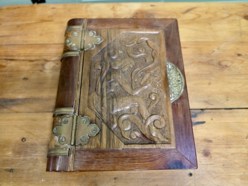 An Art Nouveau carved wooden book-shaped box with brass hinges featuring a relief carving of a seated figure surrounded by organic scrollwork.