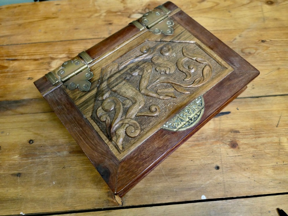An Art Nouveau carved wooden book-shaped box with brass hinges featuring a relief carving of a seated figure surrounded by organic scrollwork. View V