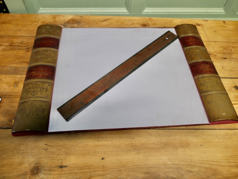 An antique leather desk blotter featuring faux book spine side borders with gold leaf tooling and a wooden ruler lying across the central pad.