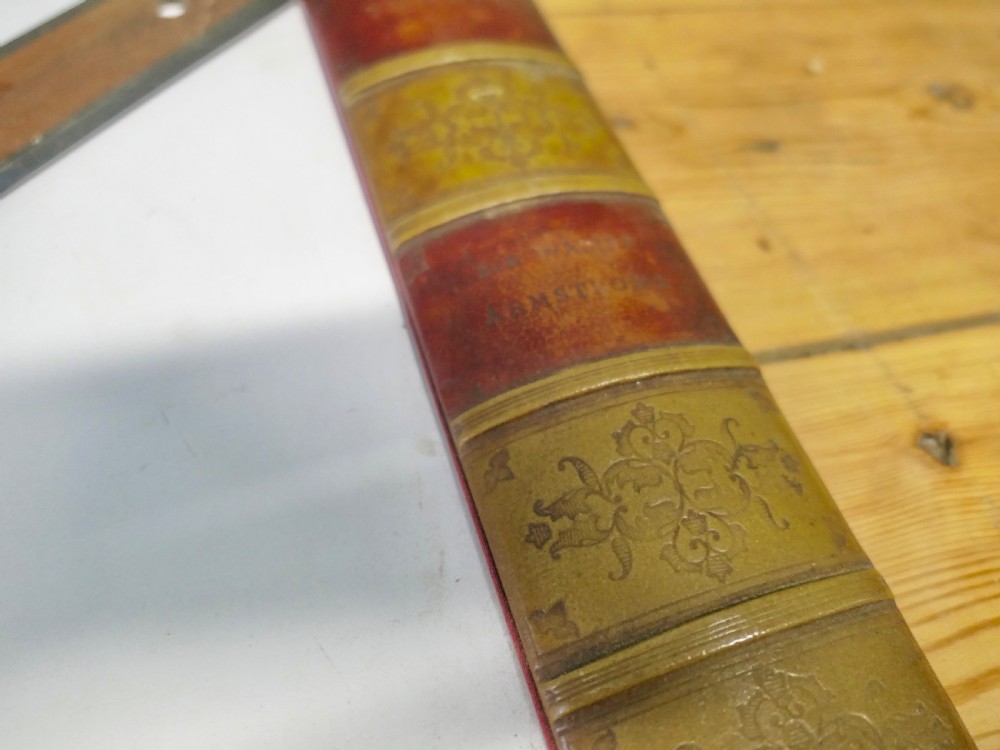 An antique leather desk blotter featuring faux book spine side borders with gold leaf tooling and a wooden ruler lying across the central pad. View V