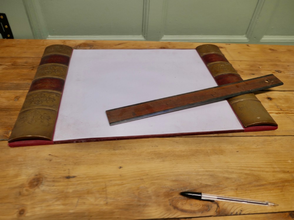 An antique leather desk blotter featuring faux book spine side borders with gold leaf tooling and a wooden ruler lying across the central pad. View VI